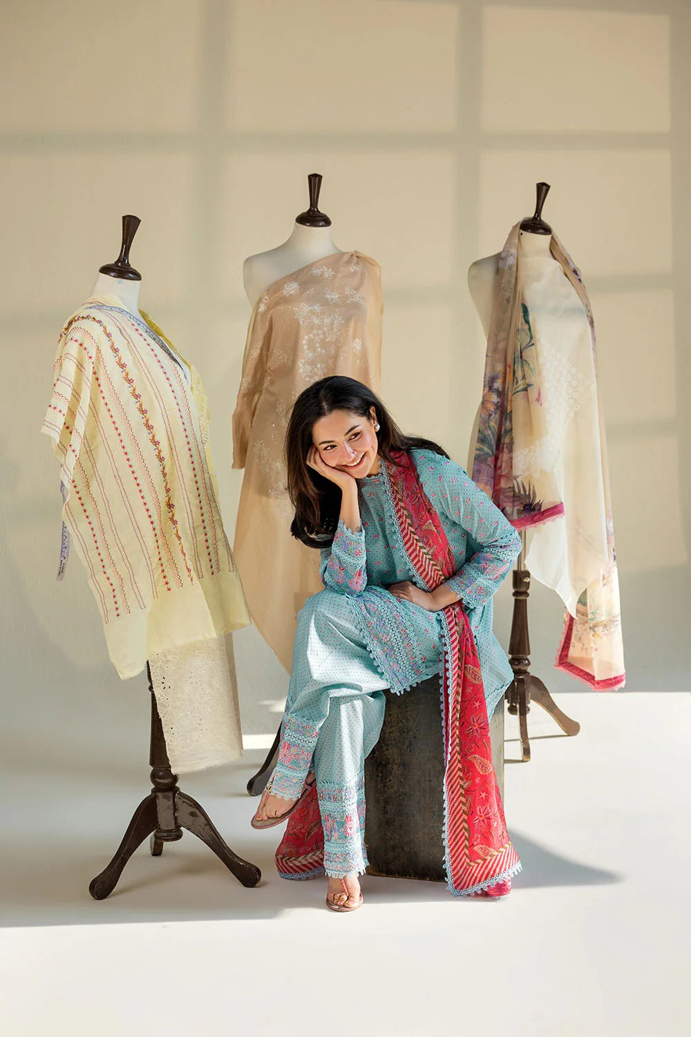 Woman sitting on a stool with traditional attire in front of mannequins displaying similar outfits.