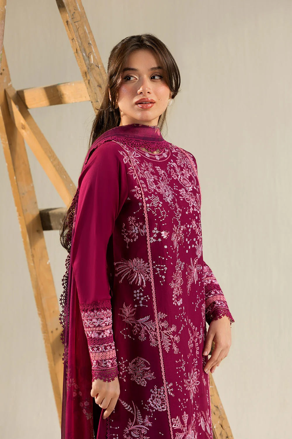 Woman wearing a maroon traditional outfit with white patterns against a neutral background