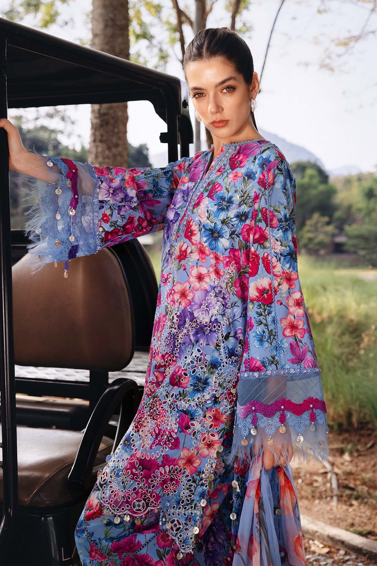 Woman in a colorful floral dress standing next to a vehicle outdoors.