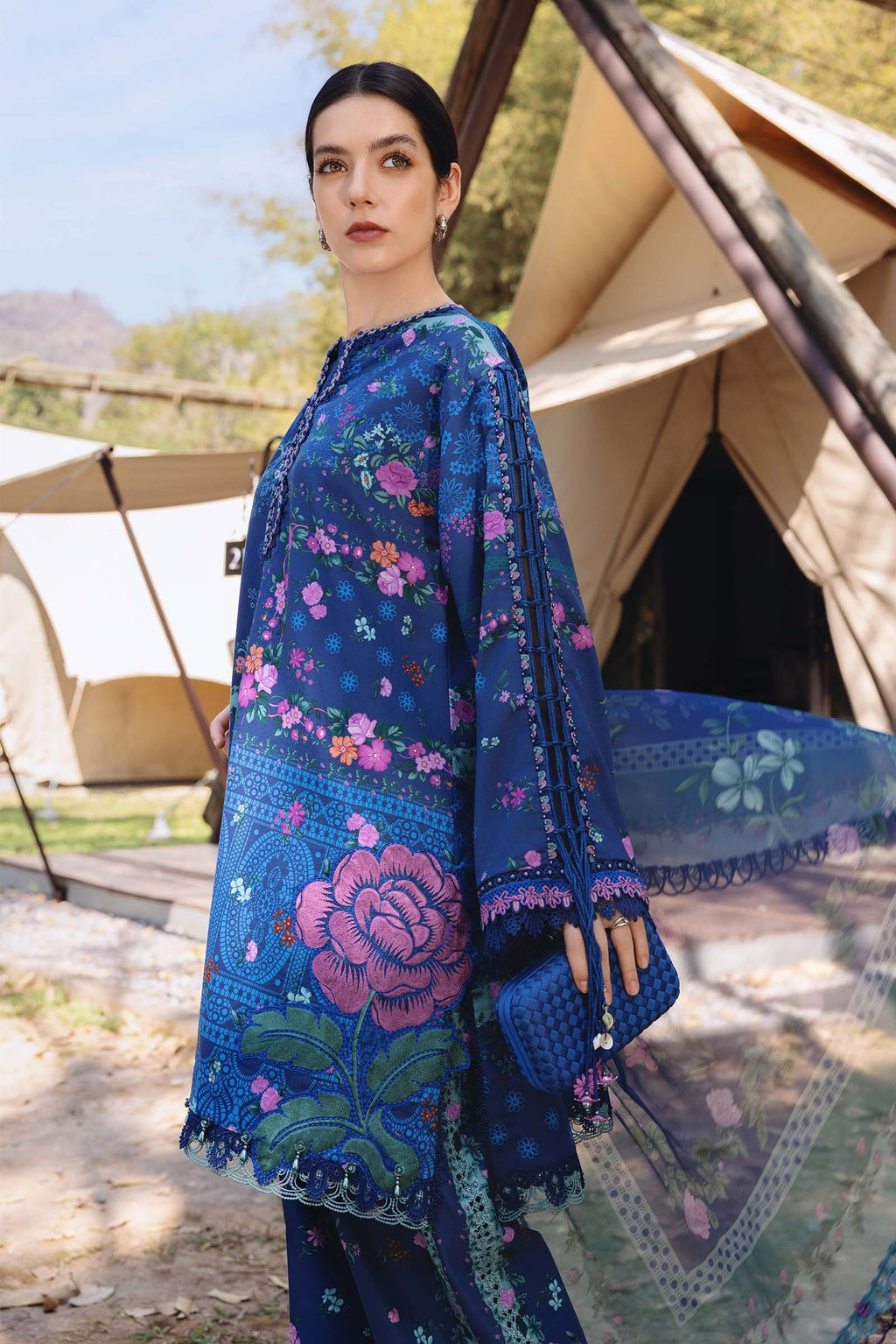 Woman wearing a blue floral embroidered dress in front of tents