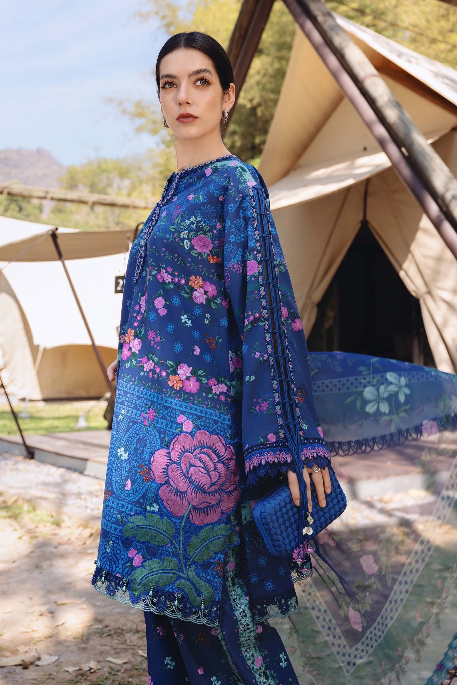 Woman wearing a blue floral embroidered dress in front of tents