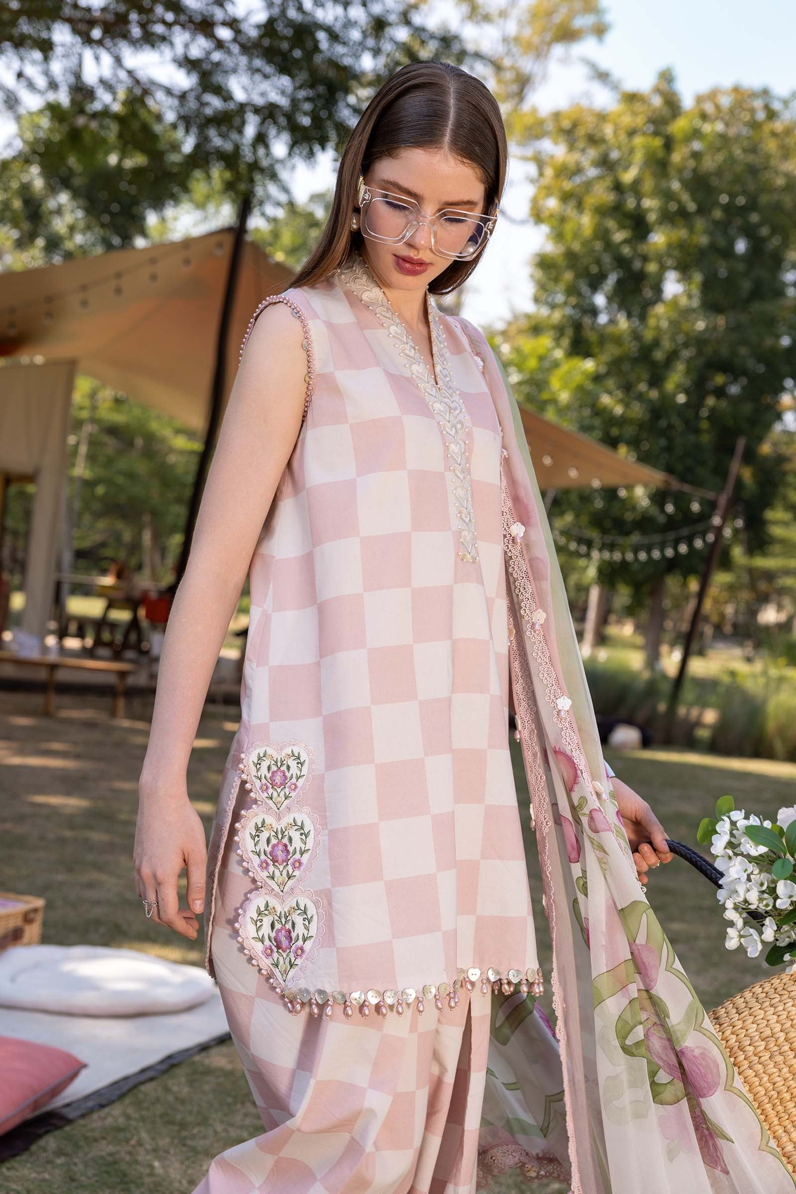 Woman wearing a pink checkered outfit with floral embroidery outdoors.