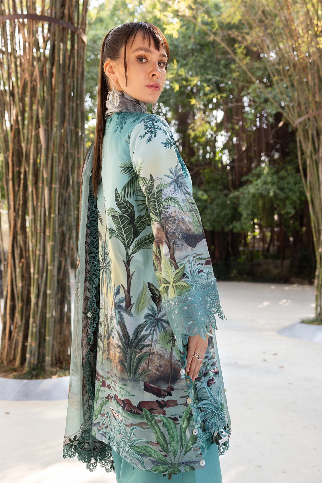 Woman wearing a floral kimono-style garment in an outdoor setting with trees and a path.