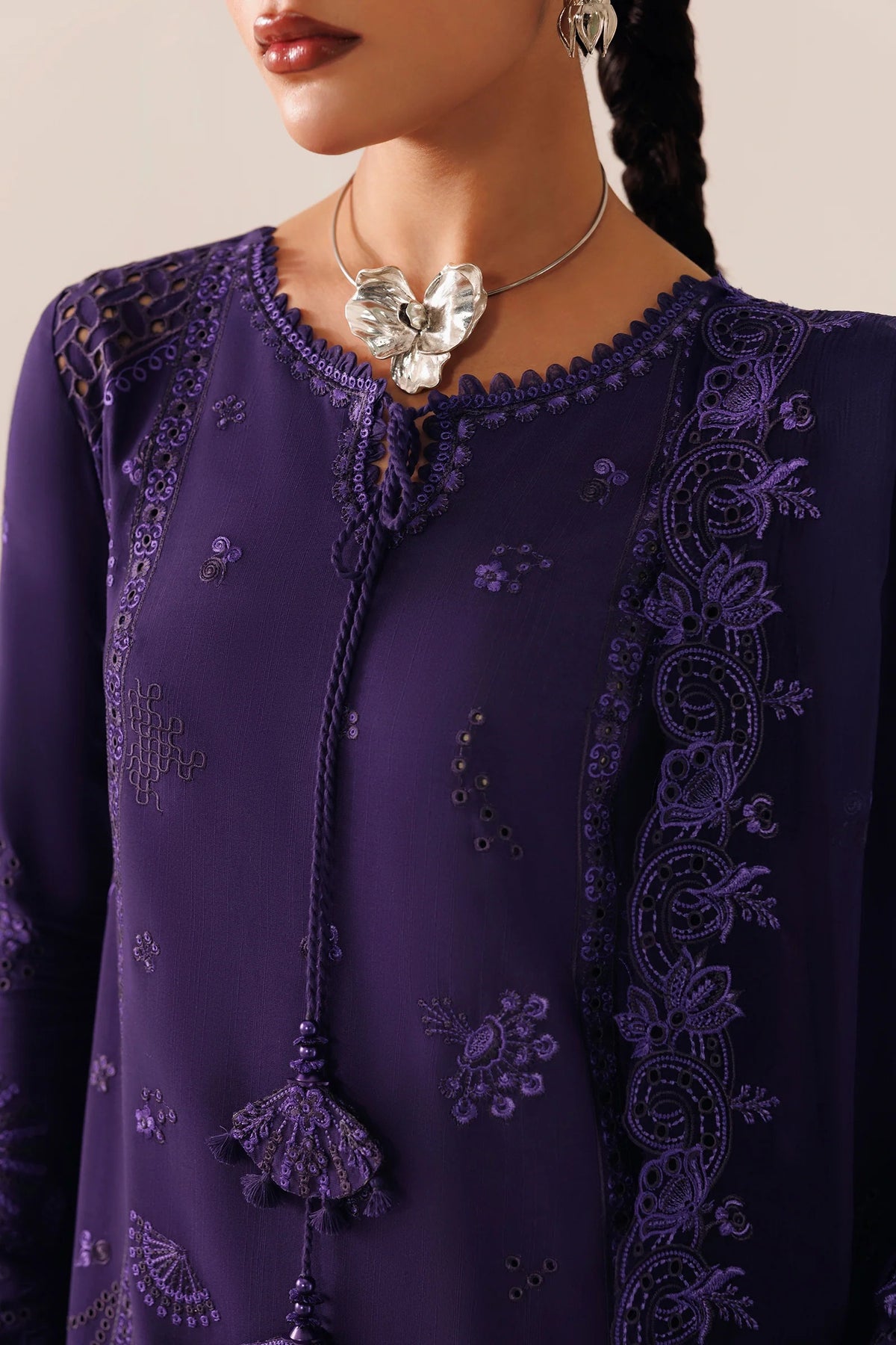 A close-up of a model wearing a deep purple embroidered tunic with intricate floral lace detailing and a butterfly-shaped silver pendant necklace.