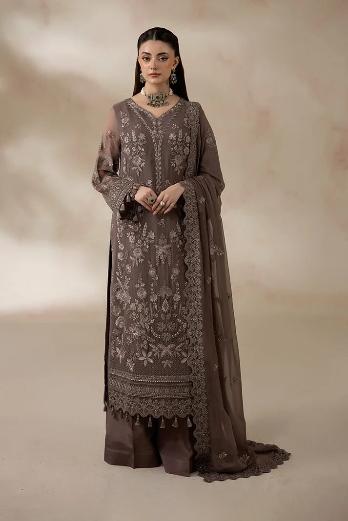 A woman models a traditional three-piece salwar kameez suit in taupe brown, featuring intricate floral embroidery on the long kurta, matching trousers, and a sheer dupatta, set against a warm beige studio backdrop.