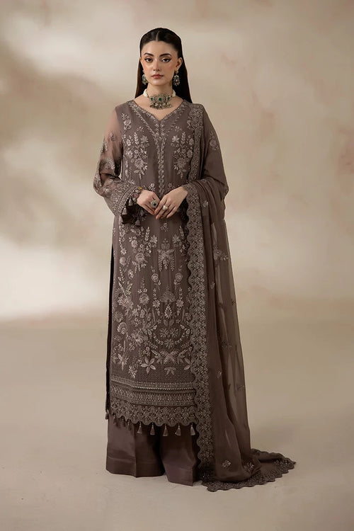 A woman models a traditional three-piece salwar kameez suit in taupe brown, featuring intricate floral embroidery on the long kurta, matching trousers, and a sheer dupatta, set against a warm beige studio backdrop.