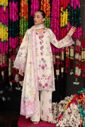 A model wearing a cream-colored embroidered traditional outfit with pink floral patterns and a matching dupatta, standing in front of a vibrant background of hanging flower garlands.