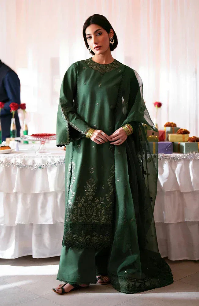A woman models a dark green traditional outfit with gold embroidery, wide-leg pants, and a matching sheer dupatta in an indoor event setting.