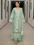 A woman models a mint green traditional embroidered dress with matching pants and a sheer matching jacket in a hallway setting.