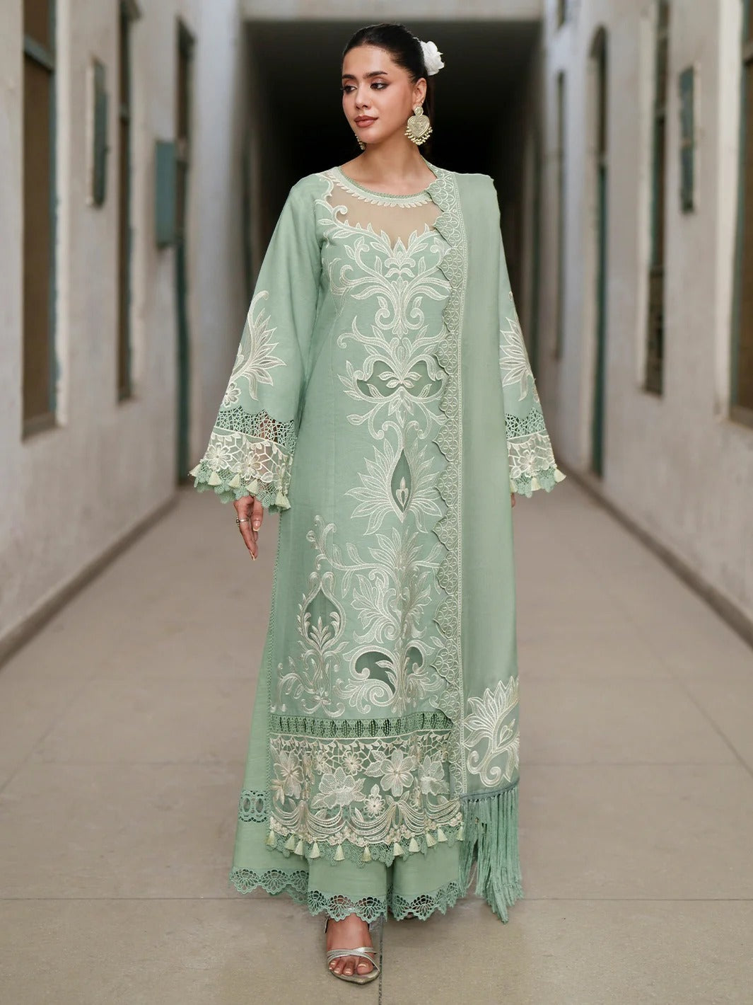 A woman models a mint green traditional embroidered dress with matching pants and a sheer matching jacket in a hallway setting.