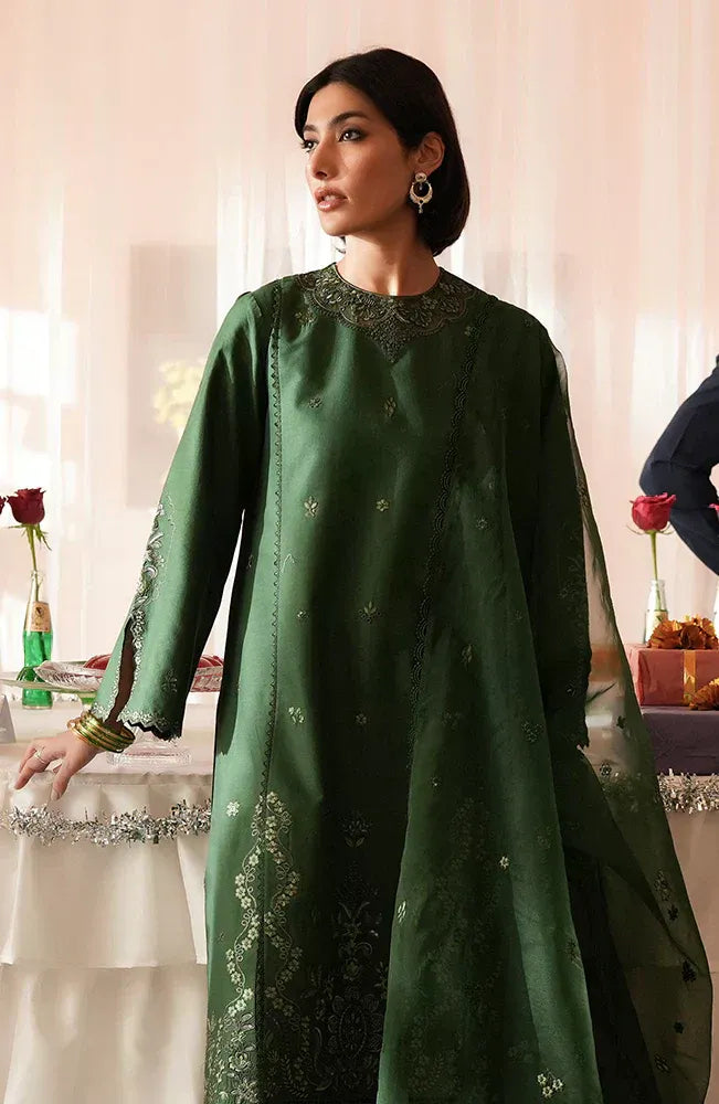 A woman models a dark green traditional long kurta set with intricate silver embroidery and sheer sleeves, set against a softly lit indoor background with decorative red roses.