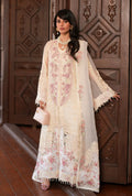 A woman models a traditional cream-colored embroidered Anarkali gown with pink floral patterns and a matching sheer dupatta, standing in front of an ornate dark wood door.