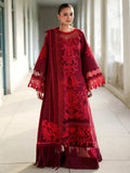 A woman models a deep red embroidered traditional dress with matching dupatta in a bright, sunlit corridor.