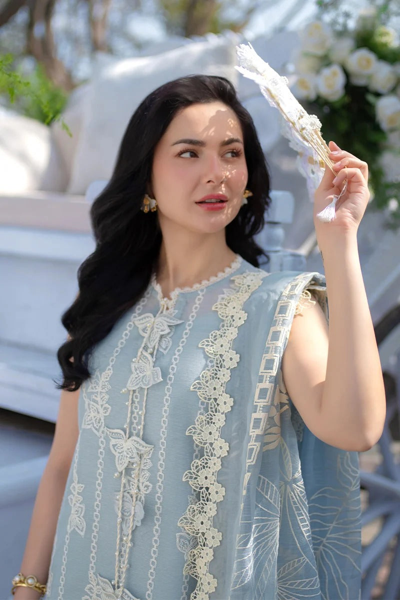 Woman in a light blue dress with lace details holding a decorative item outdoors.
