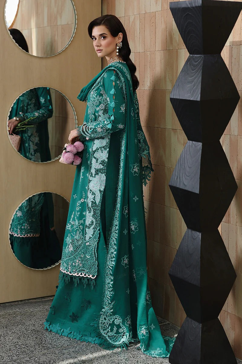 Woman in a teal embroidered outfit standing in front of a geometric wall design.