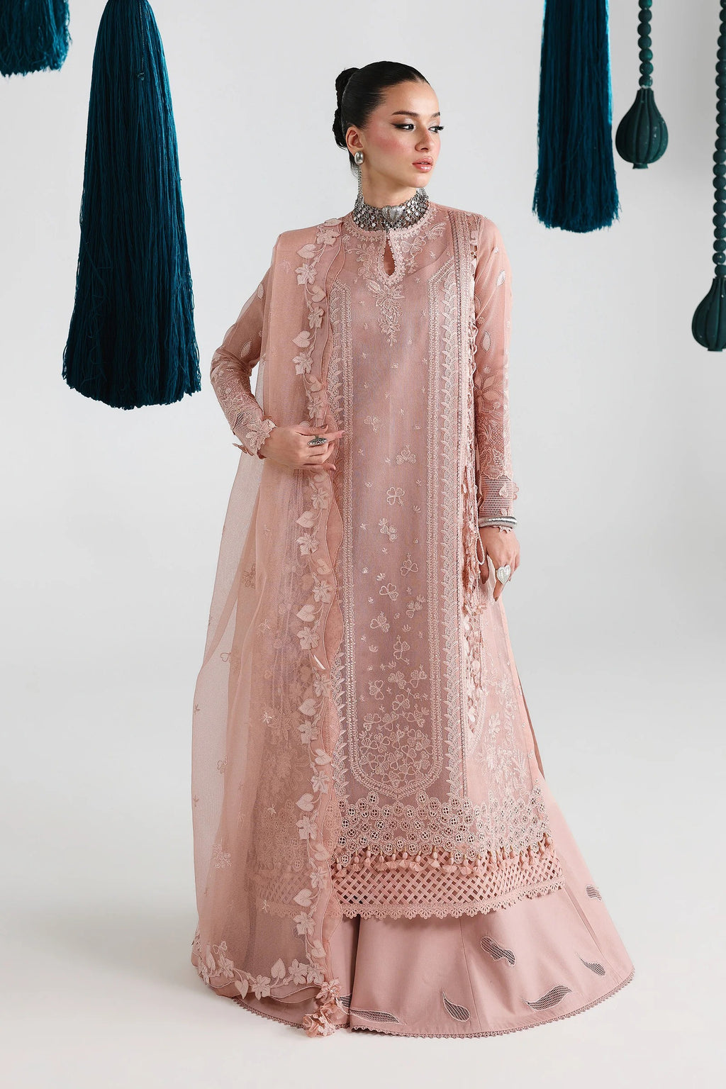 Woman wearing a pink embroidered traditional outfit with hanging green fabric in the background