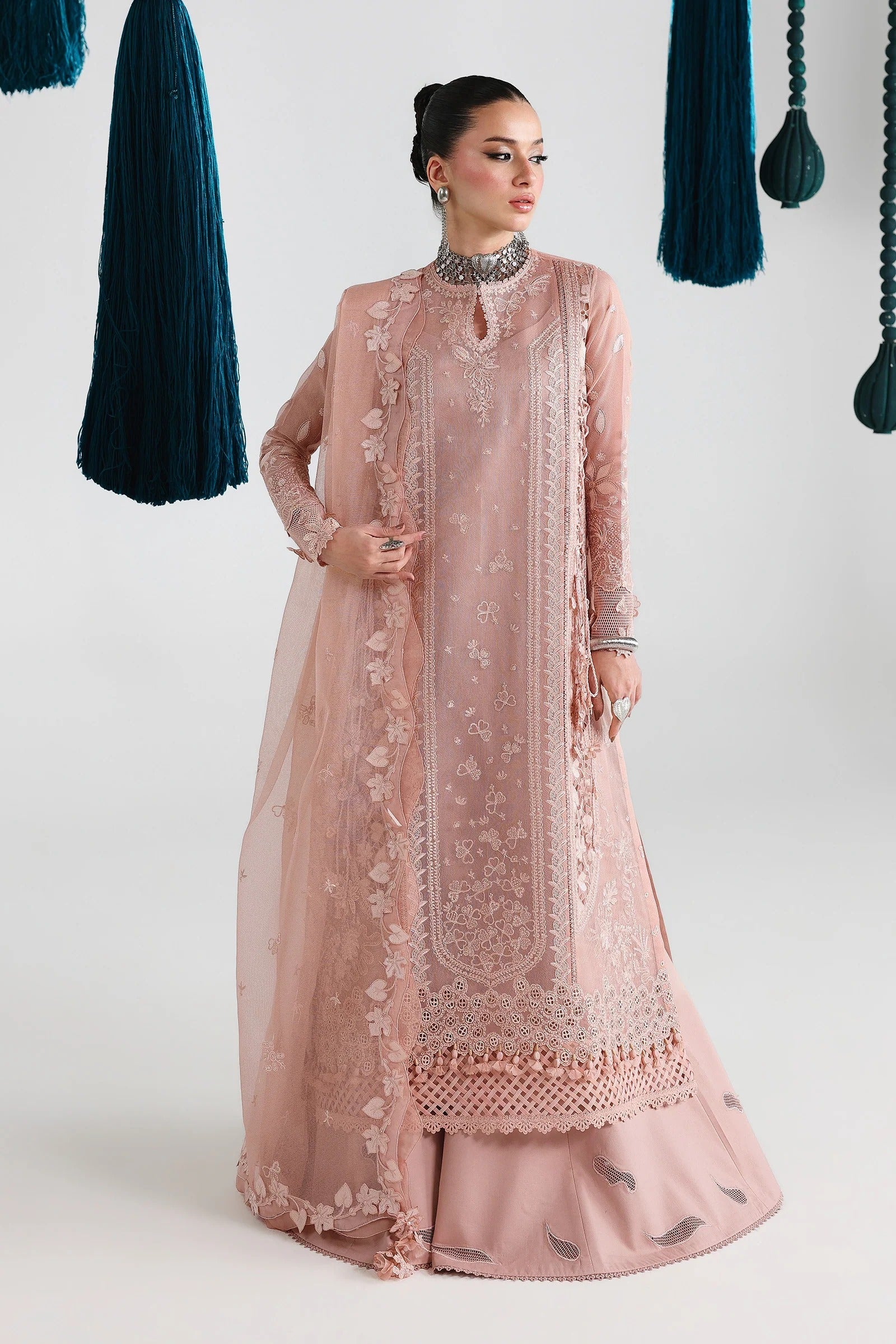 Woman wearing a pink embroidered traditional outfit with hanging green fabric in the background