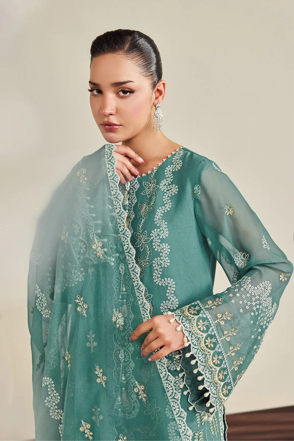 A woman modeling a teal green embroidered traditional outfit with a matching sheer dupatta, featuring intricate gold and white floral embroidery and lace borders.