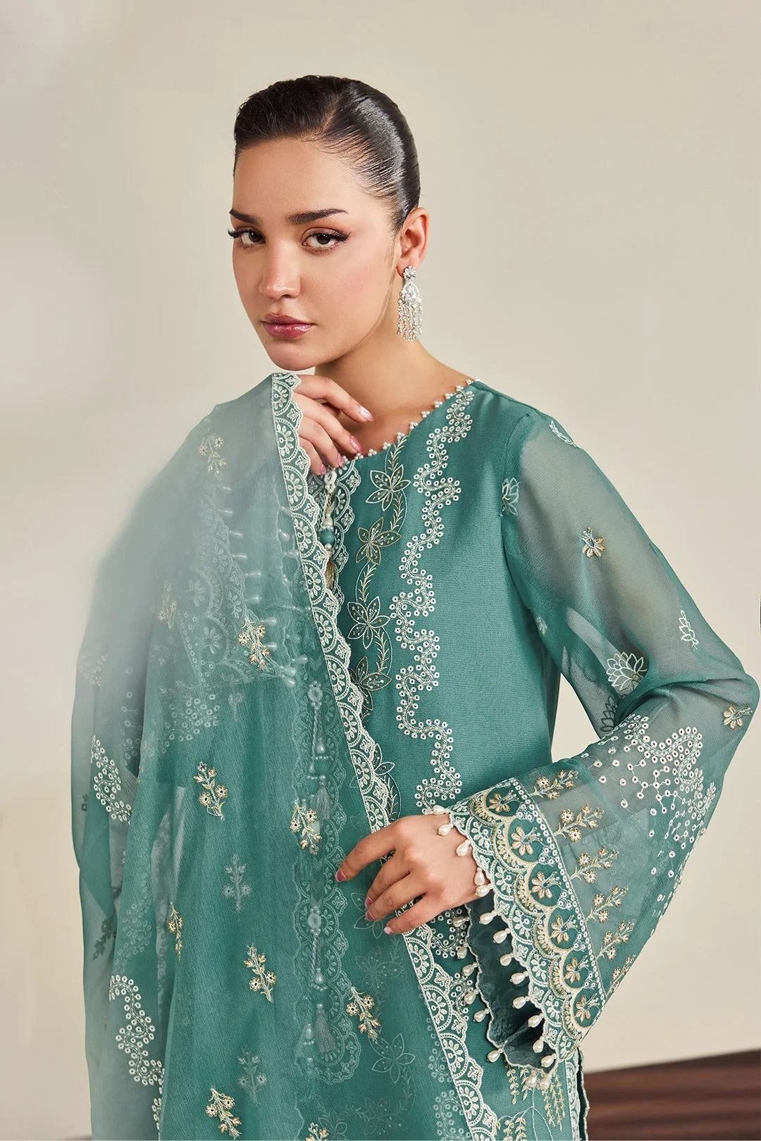 A woman modeling a teal green embroidered traditional outfit with a matching sheer dupatta, featuring intricate gold and white floral embroidery and lace borders.