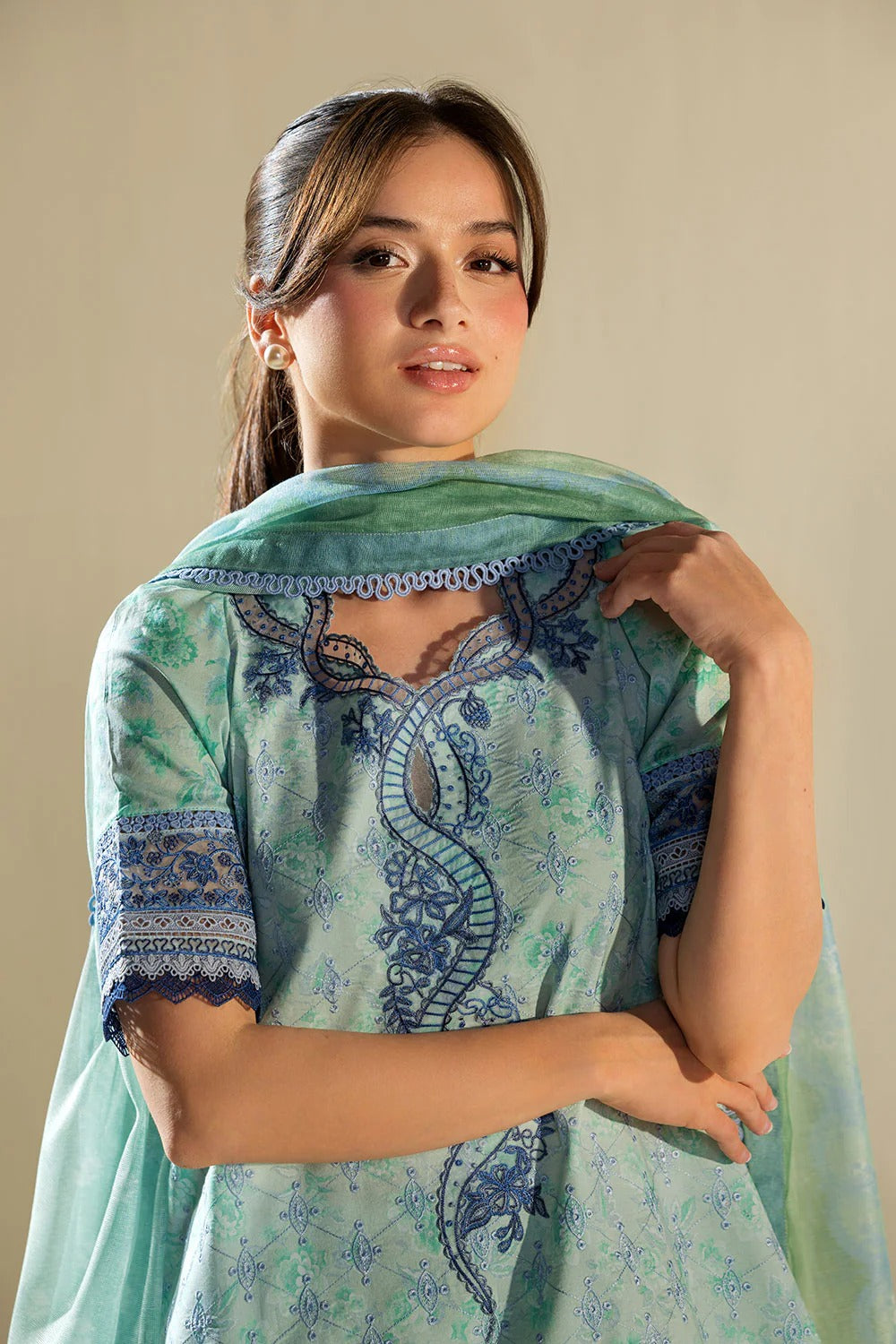 Woman wearing a light blue and green traditional outfit with intricate patterns.