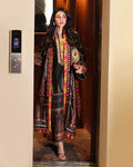 A woman wearing a traditional South Asian outfit with a long multicolor printed outer robe over a black kurta and matching trousers, standing in an elevator.