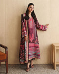 A woman models a traditional South Asian salwar kameez set featuring a deep maroon kurta and matching dupatta with intricate red, pink, and teal geometric and floral patterns, set against a beige paneled wall.