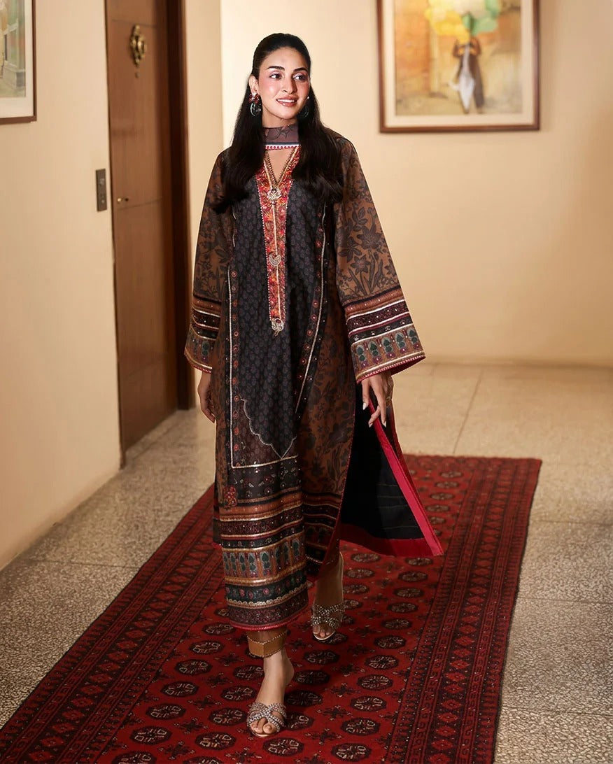 A woman models a traditional long kurta set in a hallway. The outfit features a dark brown and black patterned outer layer with red and gold embroidery on the neckline and cuffs, paired with a black and red dupatta.