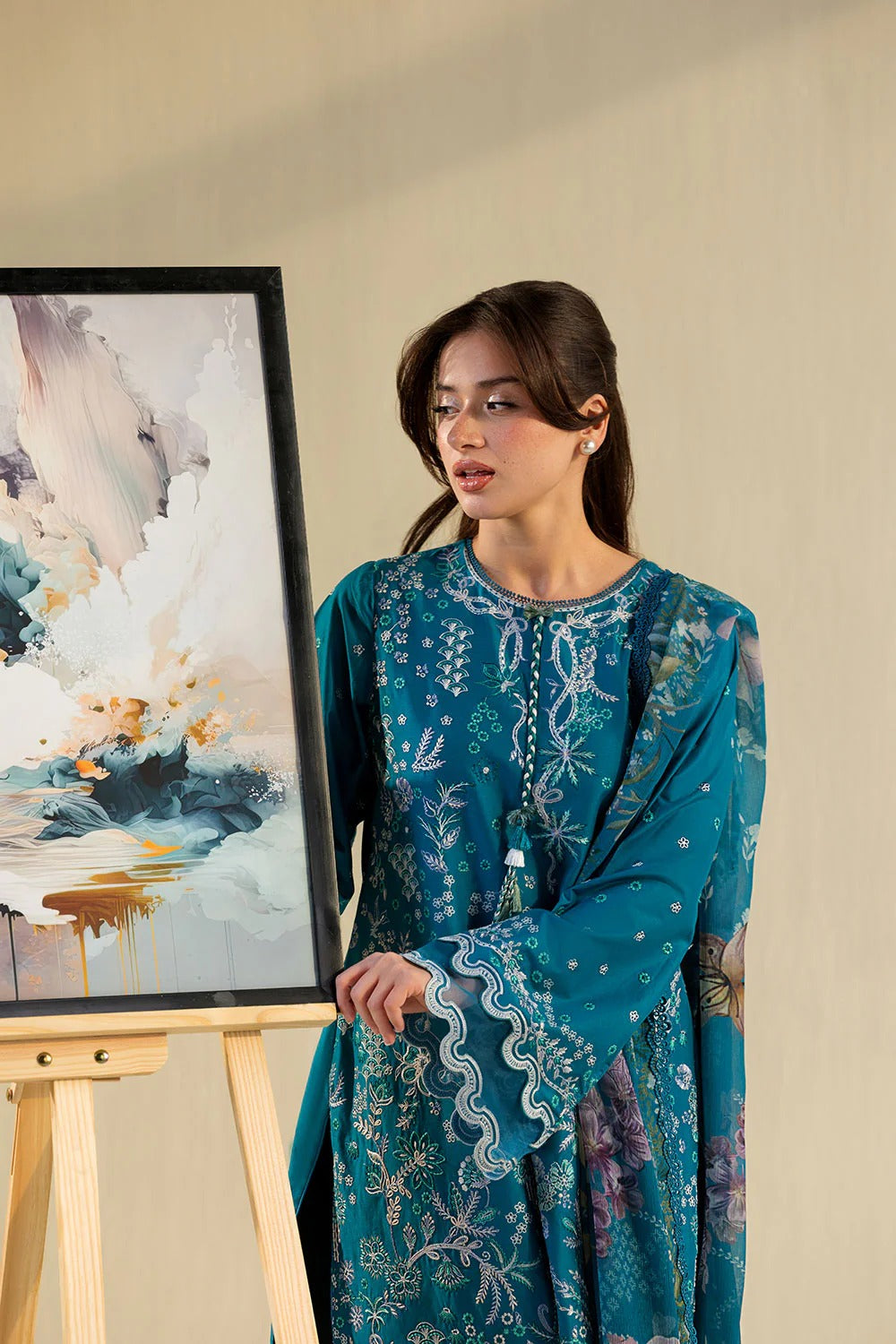 Woman in a blue patterned dress standing next to a painting