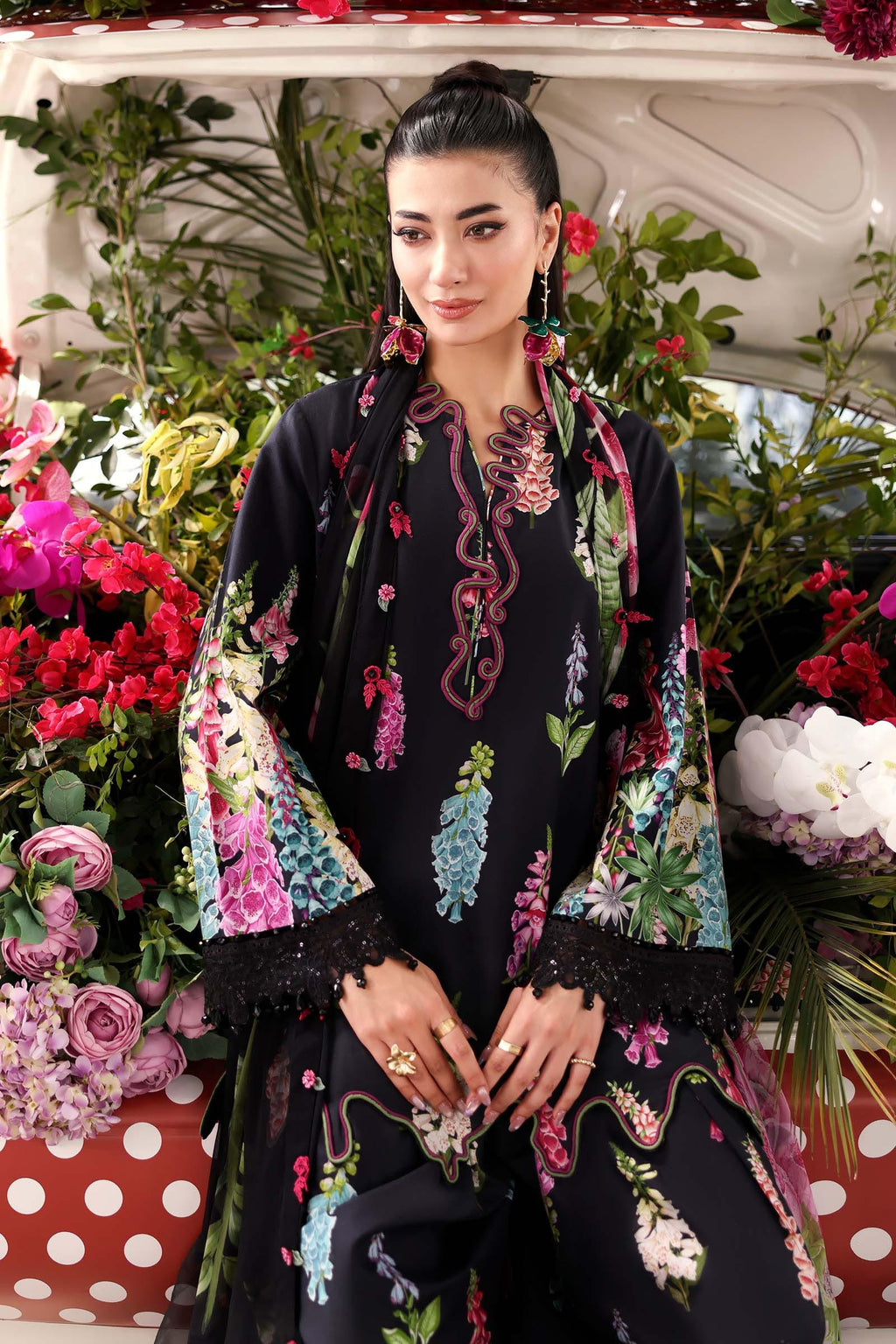 Woman in a floral embroidered outfit standing in front of a car filled with flowers.