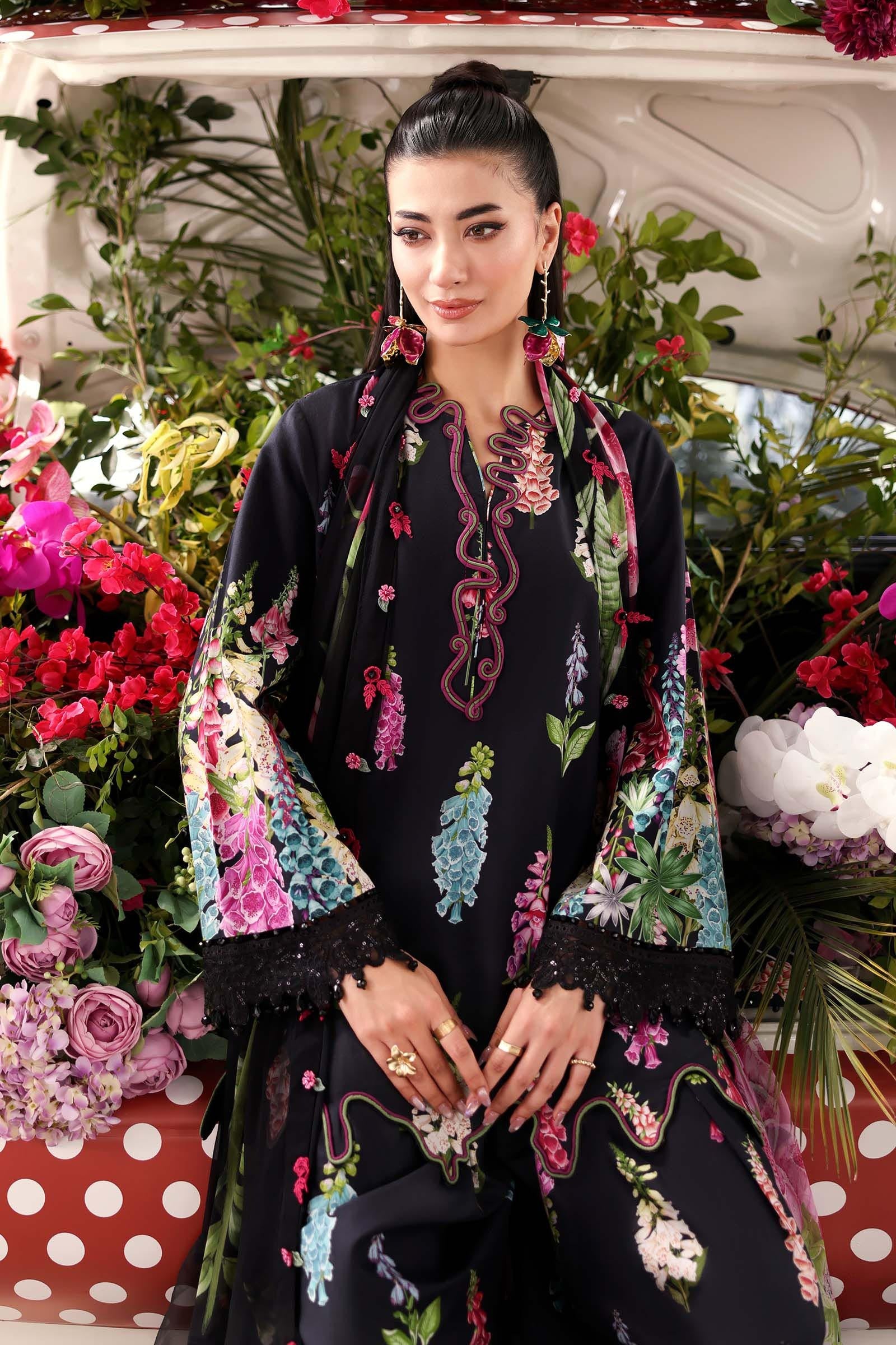 Woman in a floral embroidered outfit standing in front of a car filled with flowers.