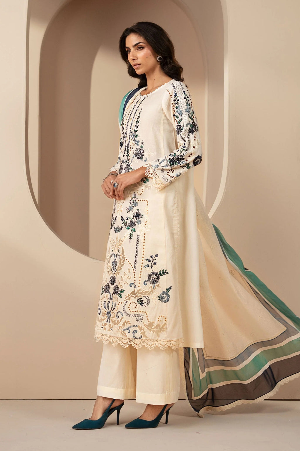 Woman wearing a cream-colored embroidered outfit with a green scarf against a beige background