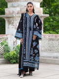 A woman models a long black embroidered kurta with intricate blue and light blue floral patterns, standing outdoors in front of a stone structure and green foliage.