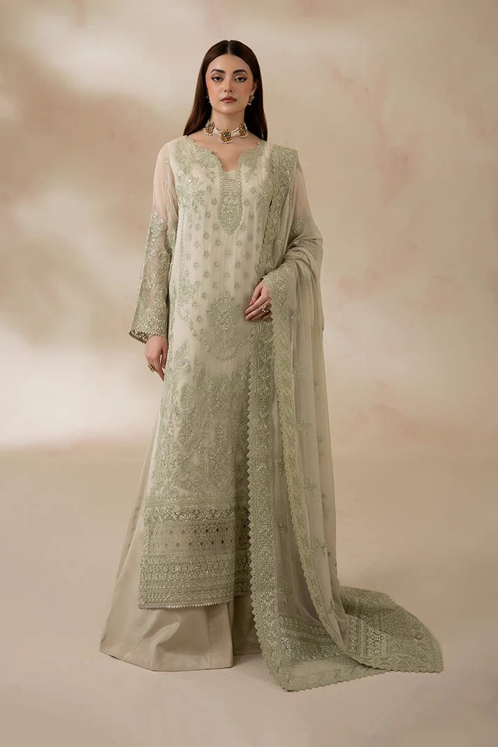 A woman models a traditional Indian outfit consisting of a light sage green embroidered kurta, matching wide-leg trousers, and a sheer dupatta, set against a soft beige background with a subtle pinkish hue.