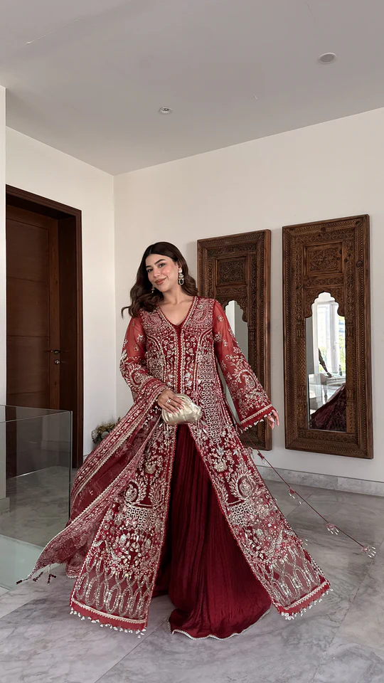 Woman in a red and gold embroidered traditional outfit standing in a room with wooden mirrors.
