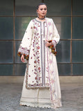 A woman models a traditional South Asian outfit featuring an off-white/cream kurta and matching trousers with intricate multicolor floral embroidery, a matching embroidered shawl, and decorative tassel trim, set against a dark paneled wall.