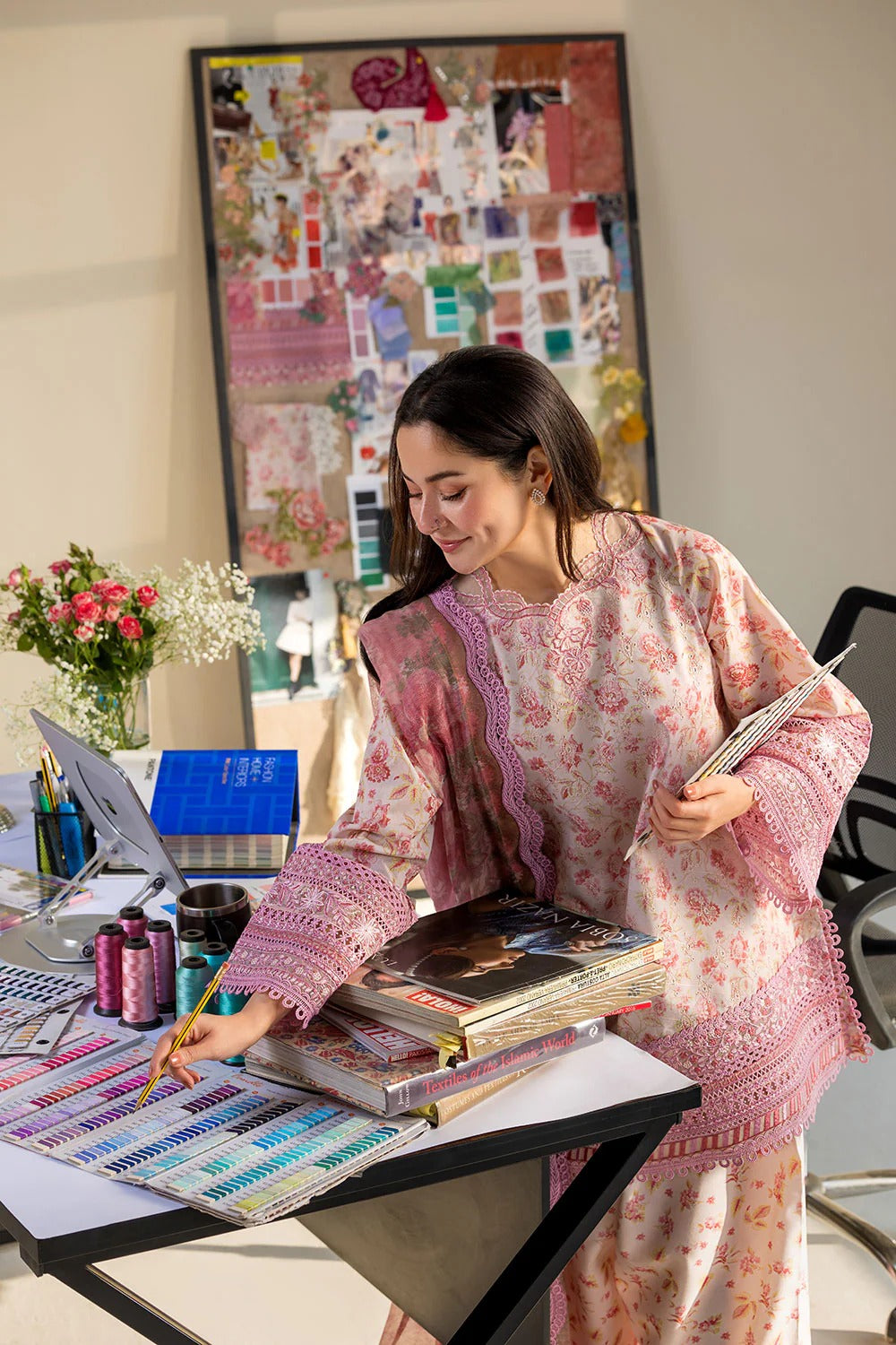 Woman in a floral dress working at a desk with books and stationery.