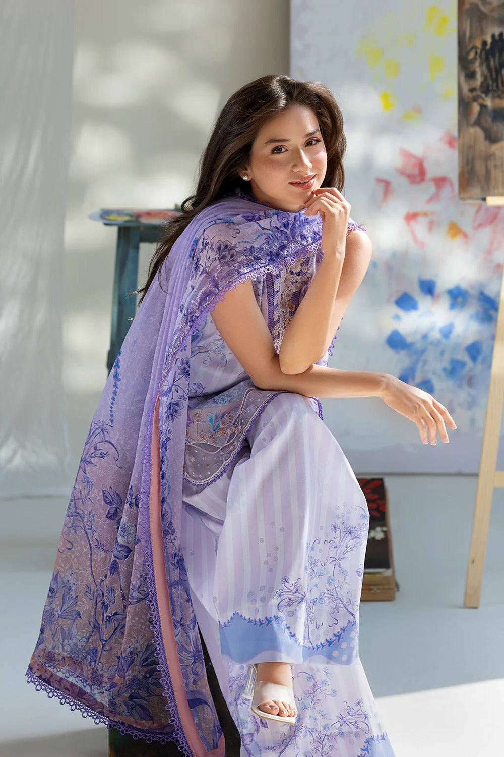 Woman wearing a light purple and white traditional outfit with a matching shawl in a room with colorful abstract art on the wall.