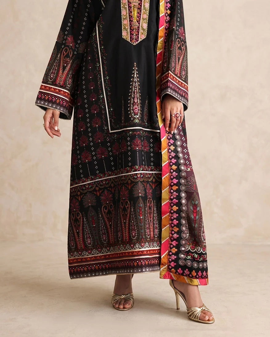 A model wearing a black embroidered traditional kurta set with wide sleeves, featuring red, gold, and white intricate patterns, paired with a matching patterned dupatta and gold heeled sandals.