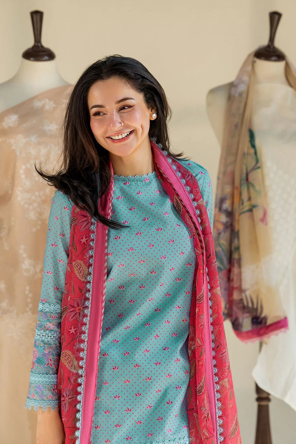 Woman wearing a teal dress with a pink scarf, standing in front of mannequins with scarves.