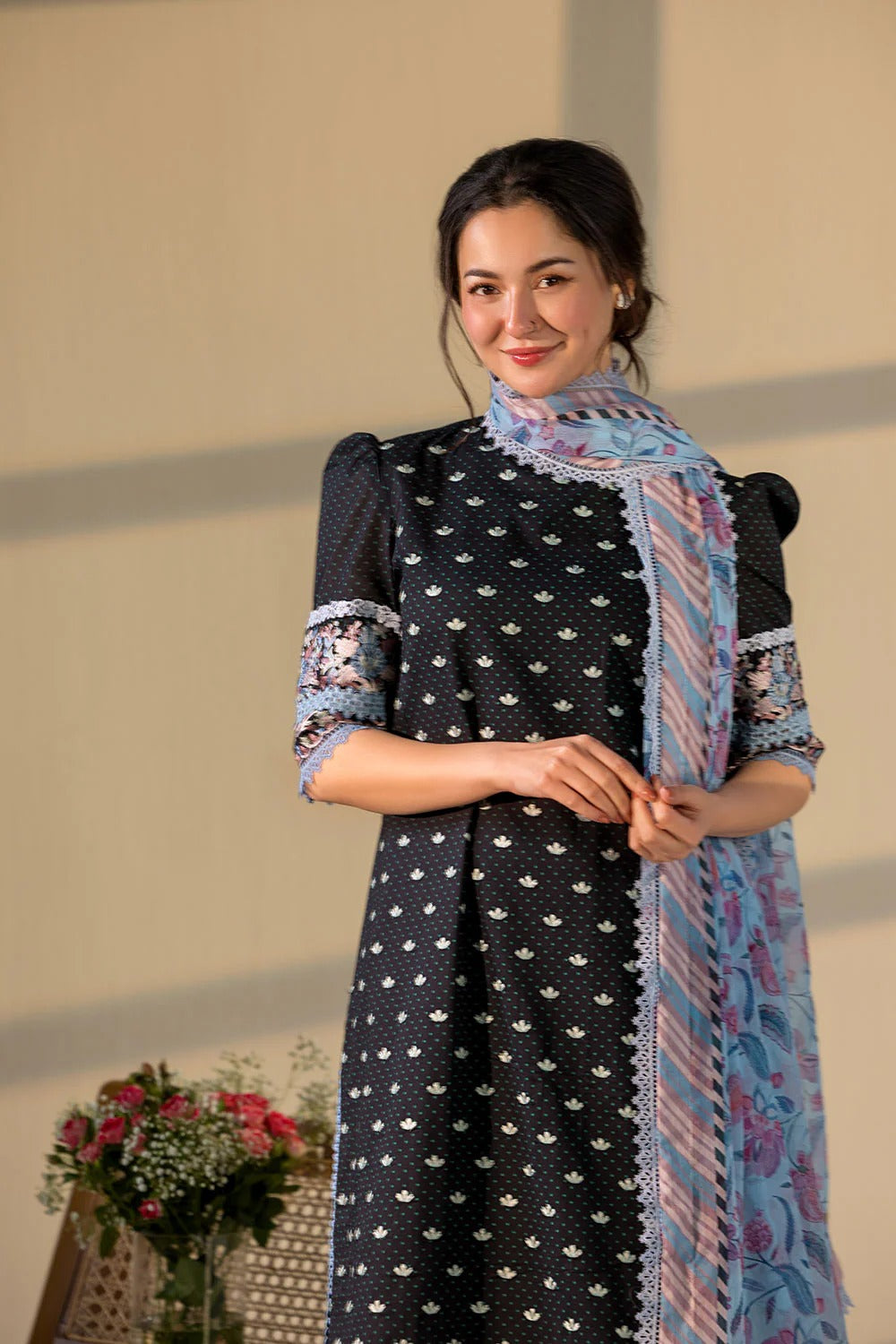 Woman wearing a black dress with white patterns and a blue floral scarf against a neutral background