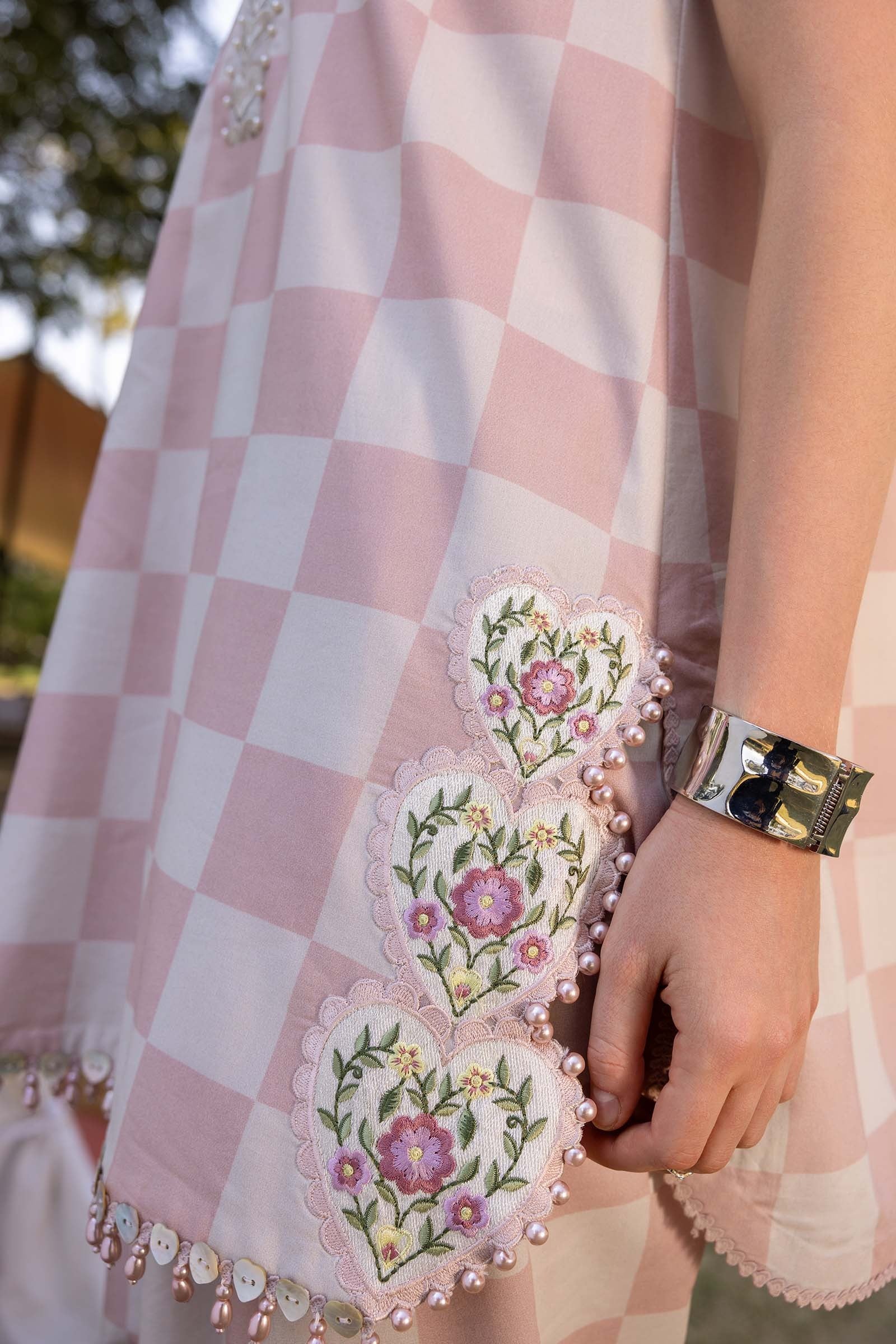 Close-up of a pink and white checkered garment with floral embroidery and a person's hand holding it.