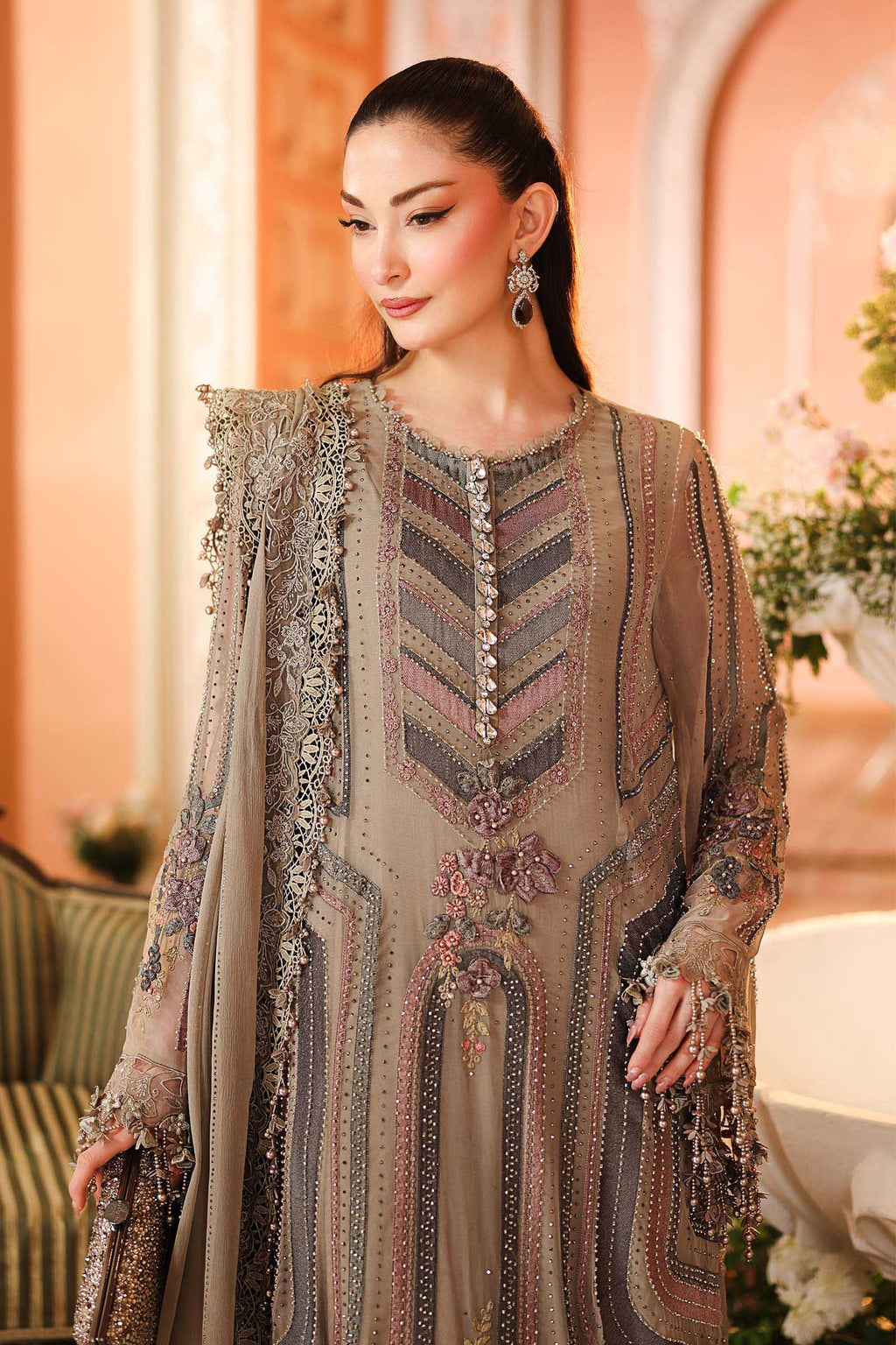 A woman models a traditional embroidered outfit with a beige tunic and matching dupatta, featuring intricate metallic and floral embroidery, in an elegant indoor setting.