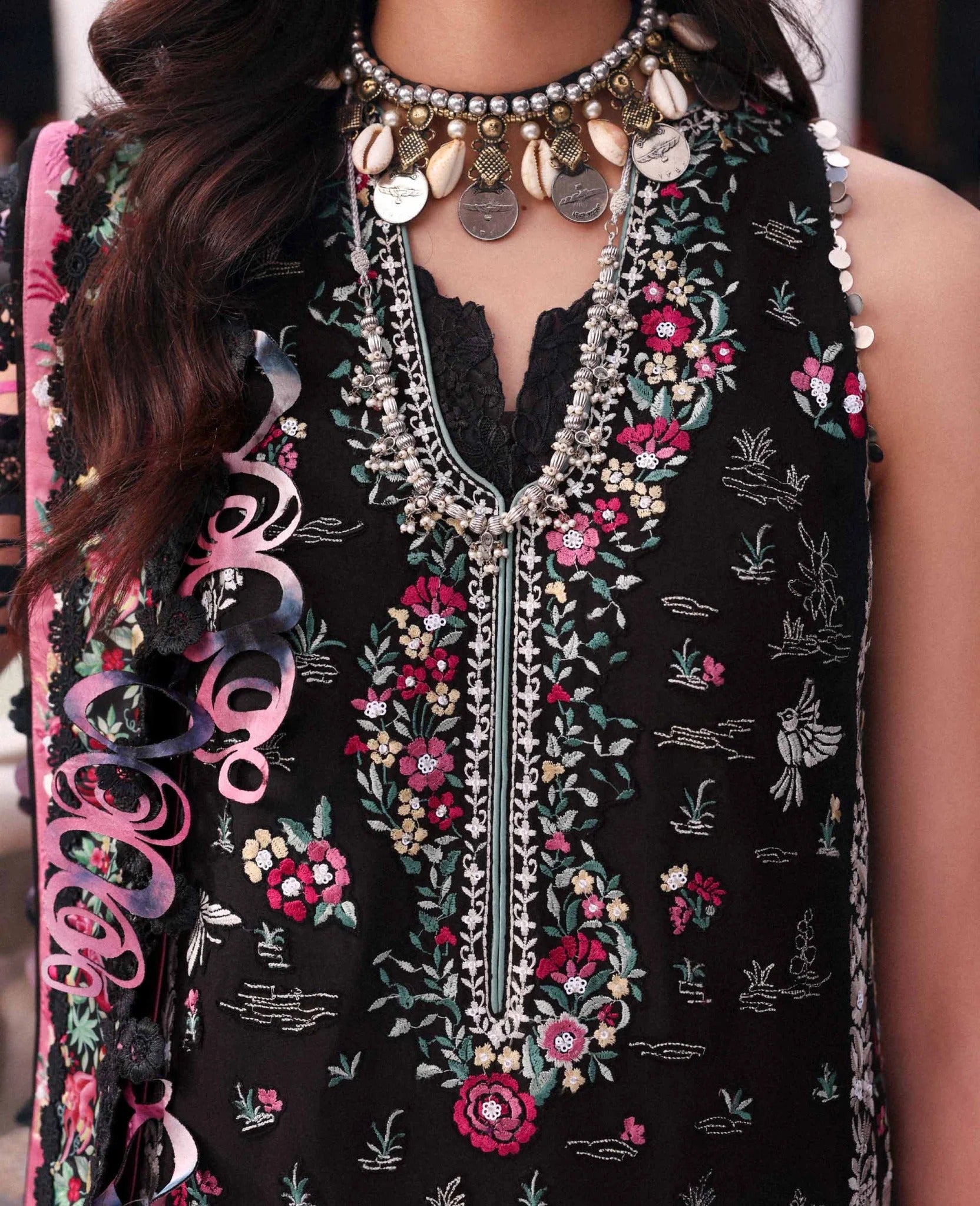 Close-up of a person wearing a black embroidered garment with floral patterns and jewelry.