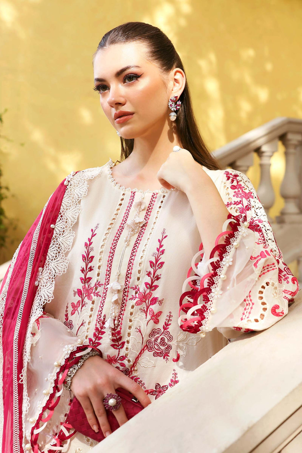 Woman wearing a traditional embroidered outfit with pink and white colors against a blurred background.