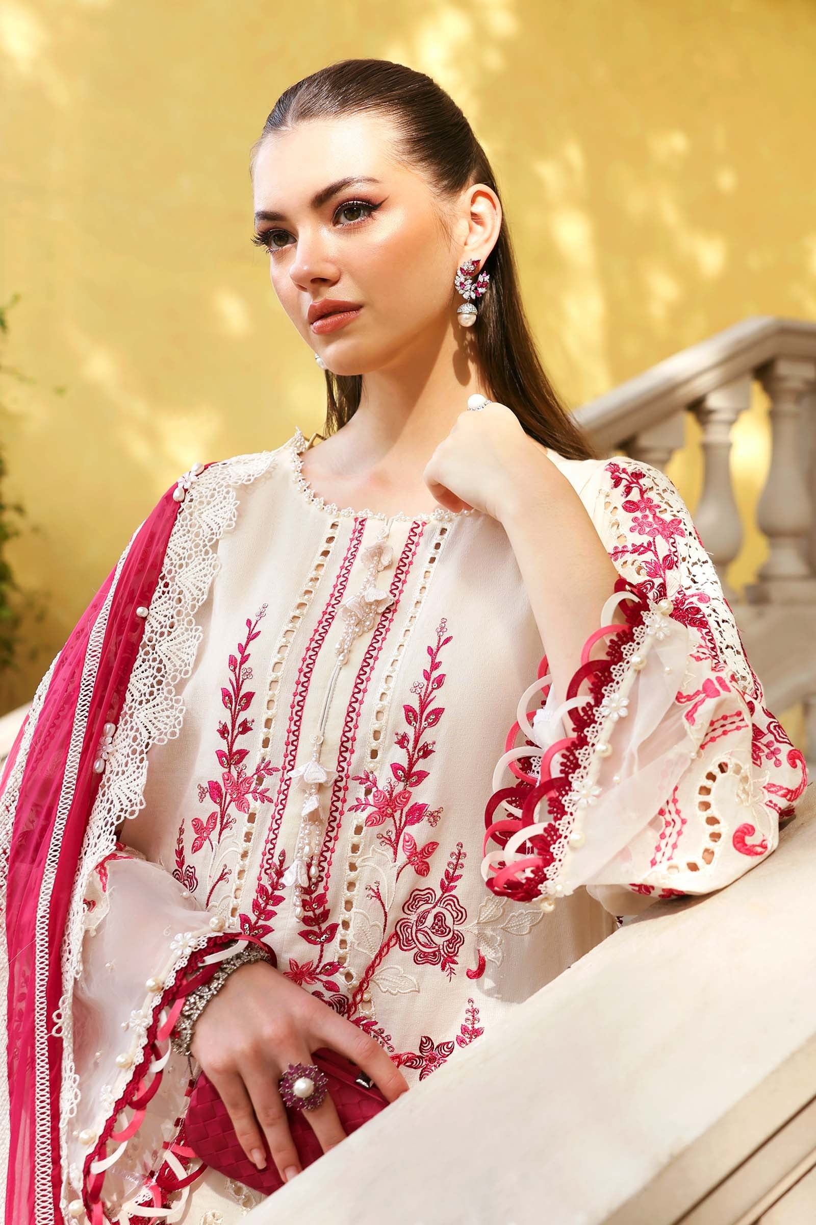 Woman wearing a traditional embroidered outfit with pink and white colors against a blurred background.
