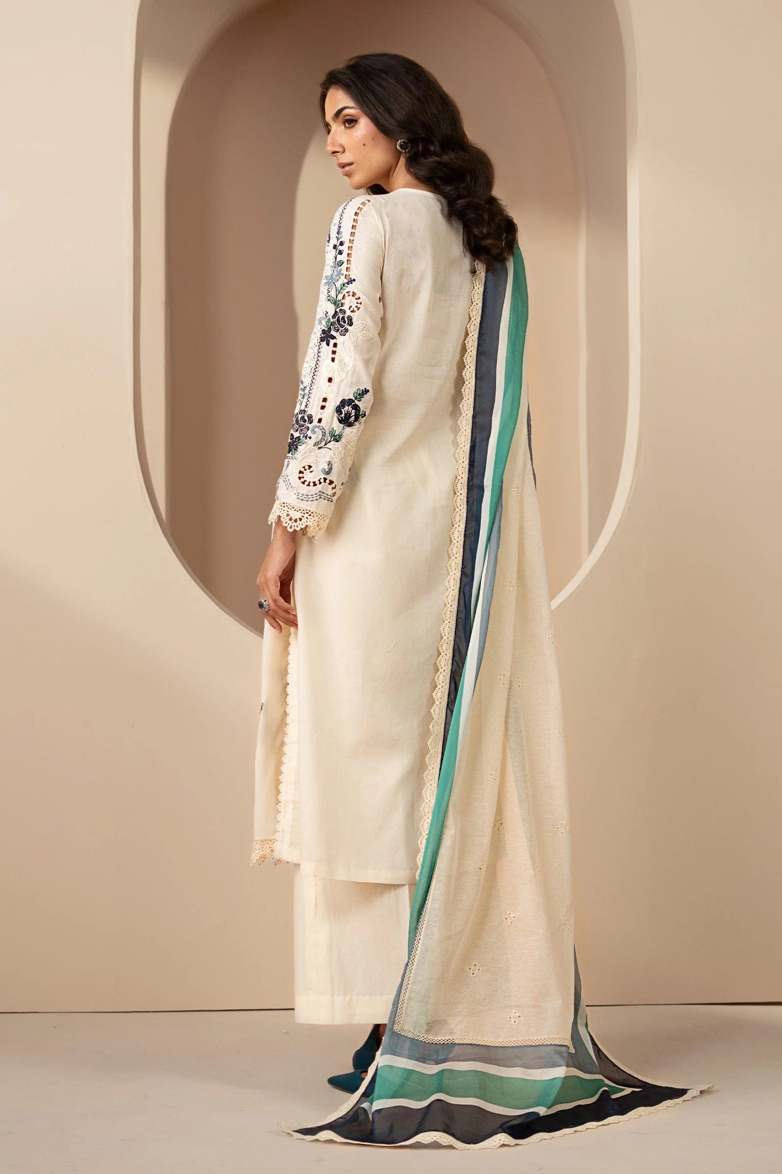 Woman wearing a cream-colored traditional outfit with floral patterns against a beige background