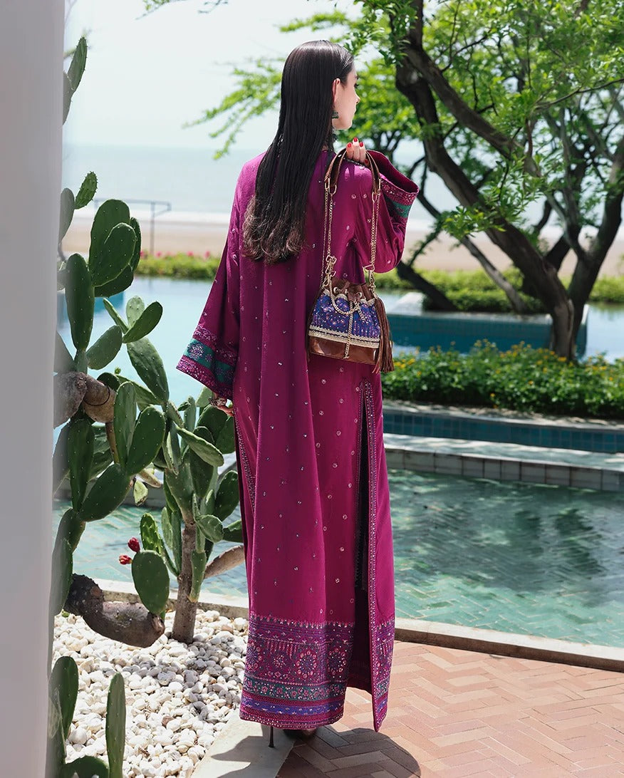 A woman stands by a poolside patio wearing a long magenta-purple embroidered robe with a matching headscarf and carrying a patterned shoulder bag. The background features a swimming pool, trees, and a distant beach.