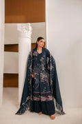 A woman models a dark navy blue traditional outfit with intricate floral embroidery and a matching sheer dupatta, standing in a minimalist interior setting with a white column.