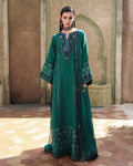 A woman models a long teal green embroidered traditional dress with wide sleeves and sheer panels, standing in front of a tiled architectural background.