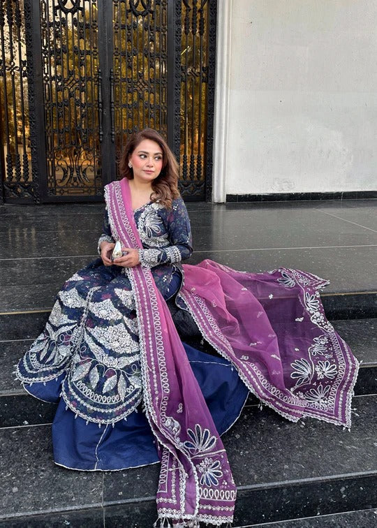Woman in traditional outfit with a purple dupatta sitting on steps.